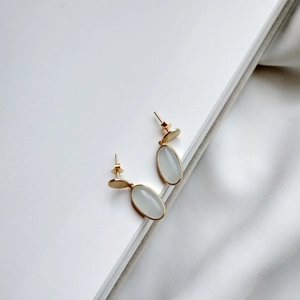 Detail of long oval gold-plated earrings with milky white opal stone inlay on white paper