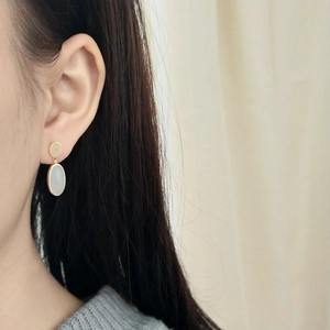 Close-up of golden oval stud earrings with white cat eye stone worn on model