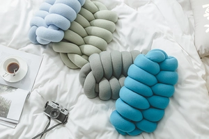 Close-up of assorted knotted knit pillows in blue and grey on white bedding