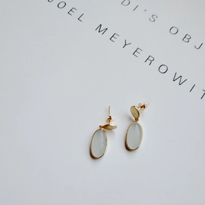 Close-up of minimalist 925 silver stud earrings with light blue stones and gold finish
