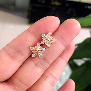 Macro shot of gold snowflake earrings with AAA zircon crystals held by hand