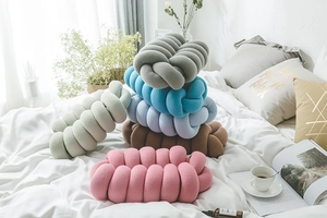 Detail of handcrafted knotted pillows in various colors on a cozy white bed setting
