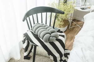 Close-up of a grey knotted decorative pillow made of plush fabric on a black chair