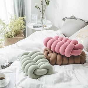 Three handmade knotted pillows in pink brown and green colors on a soft white bed