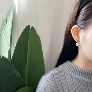 Close-up of model wearing gold brushed earrings with white oval pendant and stone