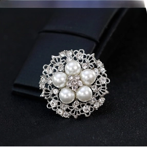 Macro shot of silver floral brooch with white pearls and sparkling crystals on black leather