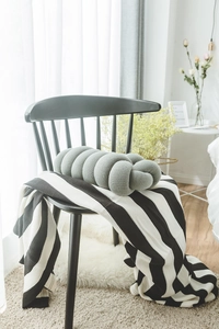 Detailed knit grey knot pillow on a black Windsor chair with a striped blanket