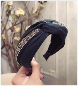 Gros plan d'un serre-tête large bleu paon en tissu avec nœud torsadé et strass brillants