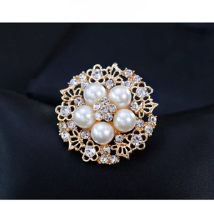 Close-up of golden floral brooch featuring five white pearls and sparkling rhinestone border