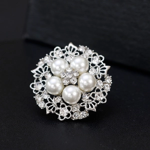Elegant silver alloy round brooch with pearls and rhinestones on a dark textured surface