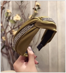 Gros plan sur un bandeau large noué vert olive orné de trois rangées de strass foncés