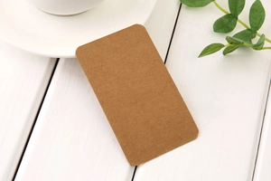 Brown kraft paper card with rounded corners on white wood background with a green leaf