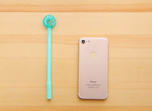 Detail of mint green donut novelty gel pen on a light wood background with a phone