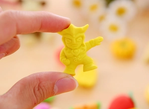 Macro view of a mini yellow rubber Ultraman eraser held between fingers