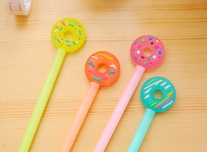 Close-up of four colorful donut-topped gel pens on a natural wooden desktop surface