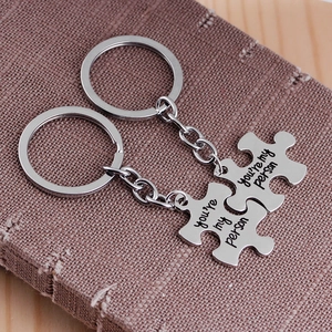Silver puzzle piece keychains engraved with 'you're my person' on a wooden surface
