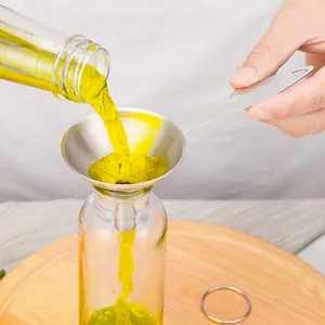 Entonnoir en inox à long manche versant de l'huile jaune d'une bouteille au récipient
