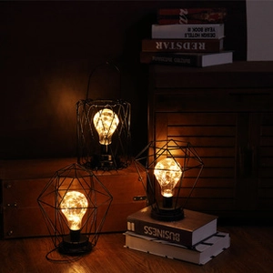 Three geometric black wire table lamps with warm LED fairy lights on decorative books