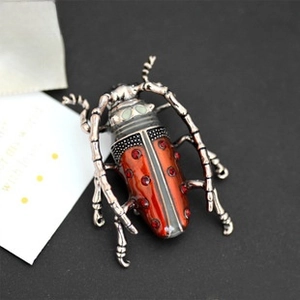 Macro detail of a beetle brooch with orange enamel finish and red rhinestones