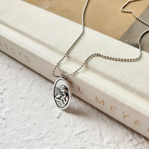 Macro detail of a vintage S925 sterling silver angel pendant on a ball chain necklace
