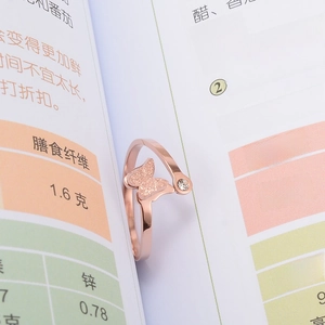Détail d'une bague papillon or rose 14k avec fini mat et zircon posée sur un livre