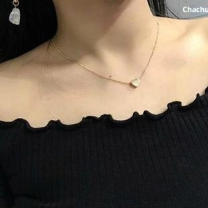 Close-up of a heart pendant necklace in gold finish worn by a model on a black top