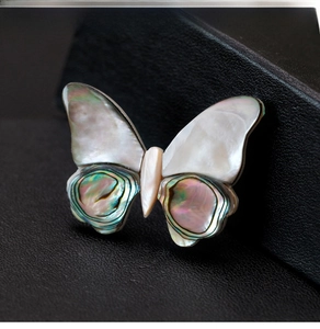 Macro shot of butterfly brooch featuring colorful iridescent shell wings on black leather