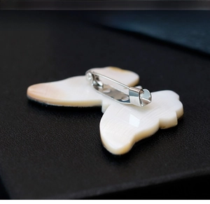 Detailed back view of a white shell butterfly brooch with a silver metal safety pin