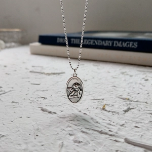 Macro detail of silver vintage angel relief pendant with beaded chain on white surface