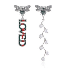 Detailed view of asymmetric bee drop earrings with red-green crystals and white pearls