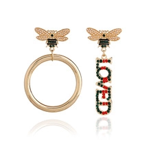 Detail of asymmetrical bee earrings with LOVED letters and red green crystals