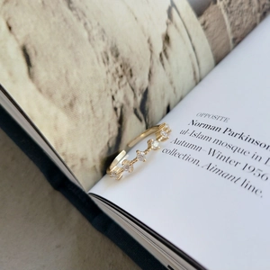 Dettaglio di un anello in oro 18 carati con cinque zirconi su sfondo di libro decorativo