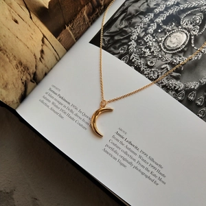 Detailed close-up of golden crescent moon pendant on fine chain over editorial book