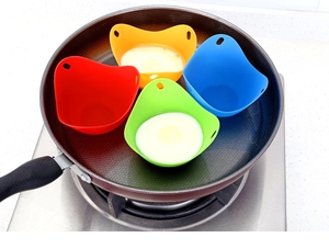 Detailed view of four colorful silicone egg poachers with raw eggs in a frying pan