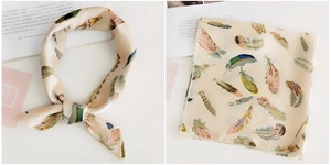 Detail of silk square scarf with colorful feather print on beige background texture