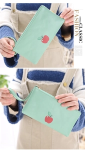 Detail of mint green cartoon apple clutch bag with zipper and wrist strap shown in use