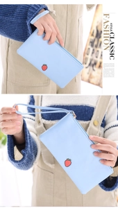 Detail of light blue leather wristlet clutch featuring embroidered strawberry pattern