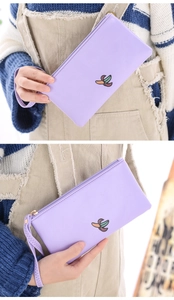 Detail of a purple fabric hand bag with banana print and wrist strap held by a model