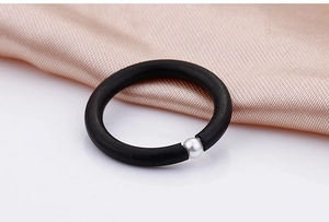 Close-up of a matte black ring with a polished silver pearl on soft champagne silk fabric