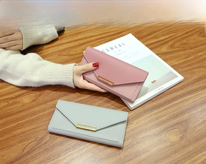 Pink and blue-grey envelope-style long wallets with gold metal buckle on a wooden desk