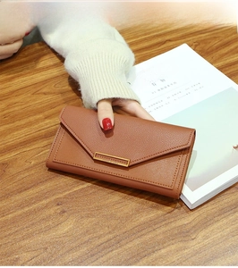 Detail of a brown leather long wallet with golden metal bar and envelope flap closure