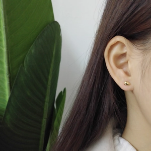 Close-up of a minimalist golden water drop stud earring worn by a model in soft light