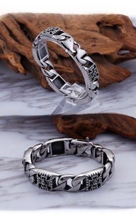Detail view of punk style stainless steel cuban link bracelet with skull cross charms