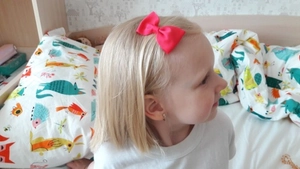 Close-up of a vibrant red grosgrain ribbon bow hair clip worn by a young child