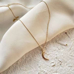 Close-up of golden moon pendant necklace elegantly draped over white silk fabric