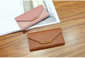 Detail of pink and brown long envelope wallets with metal bar trim on a wooden desk