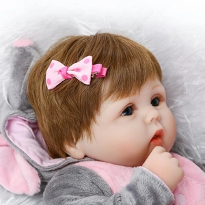 Realistic newborn baby doll with pink polka dot bow and hoodie on a soft plush blanket