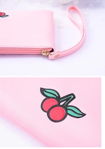 Close-up of pink leather wallet featuring cherry pattern and textured zipper strap detail