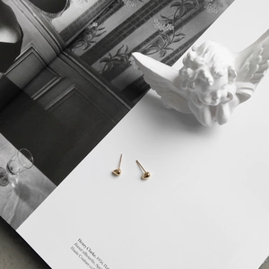 Artistic layout of golden heart stud earrings on a white book with a plaster angel statue