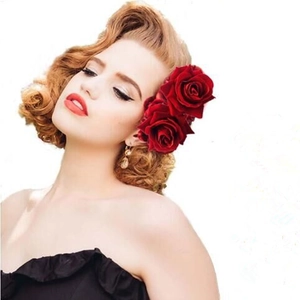 Close-up of a woman wearing double red velvet rose hair clips on retro gold curly hair